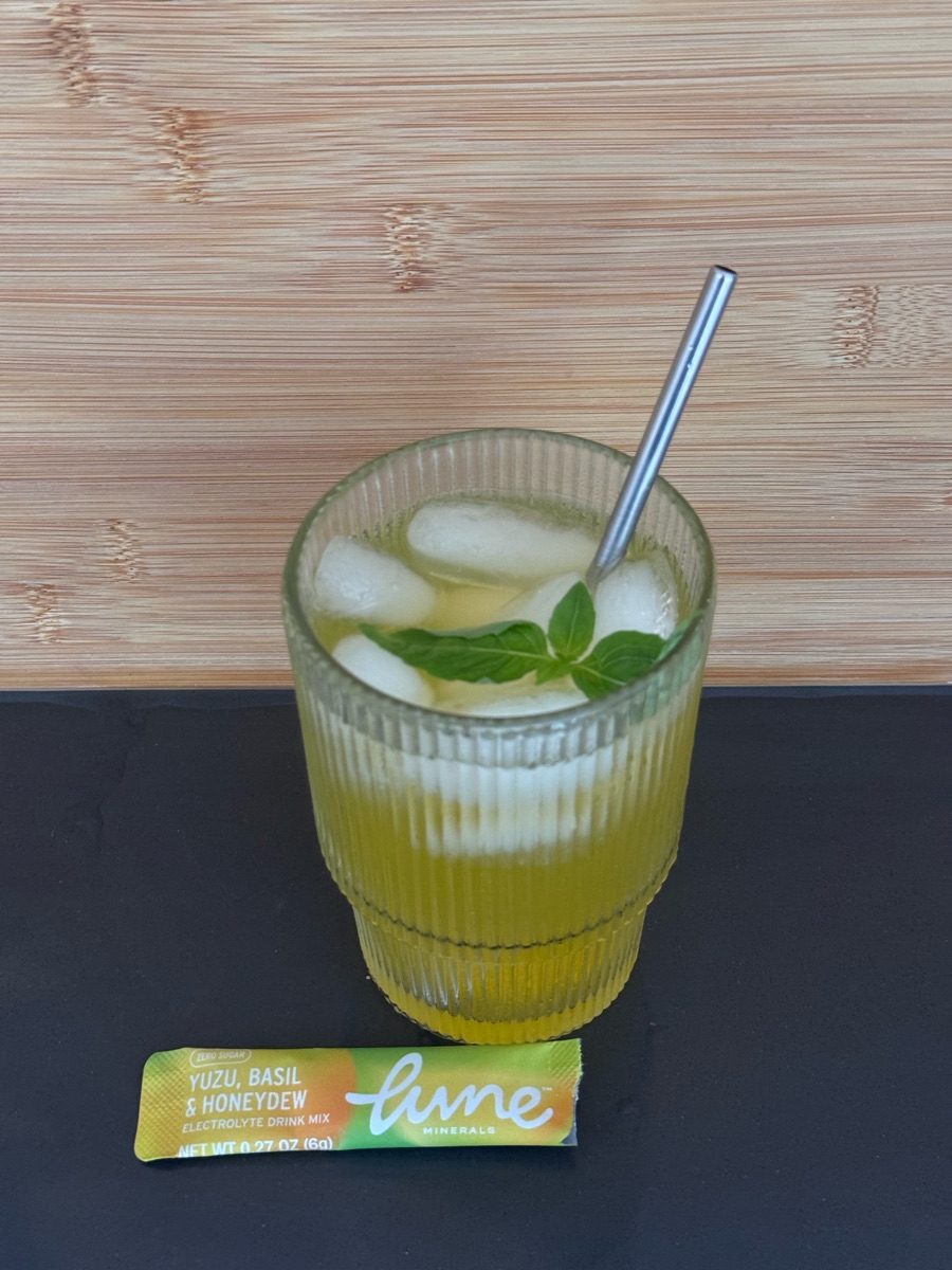 Customer photo: an iced glass of Yuzu, Basil & Honeydew with a basil sprig, next to the stick pack