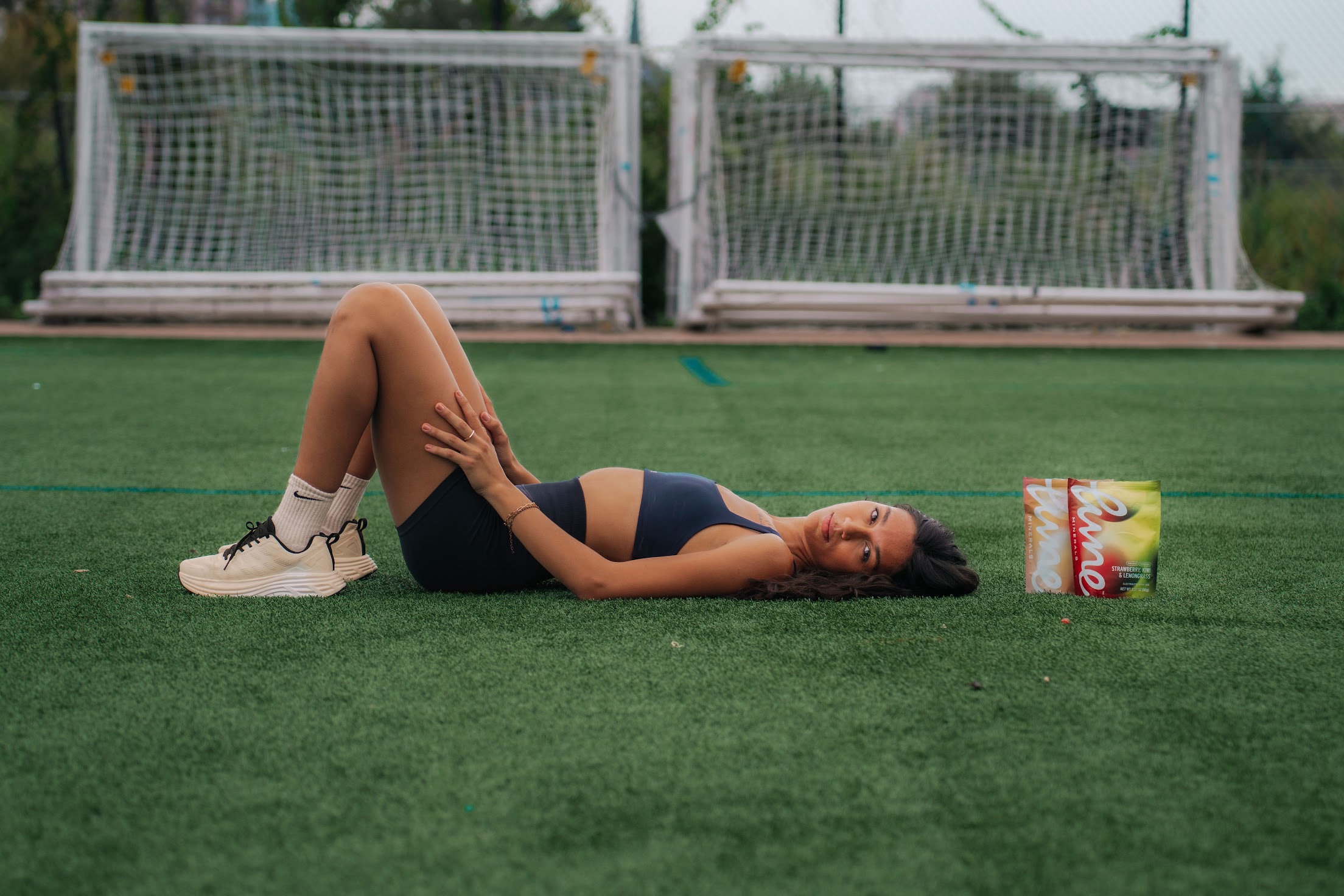 Woman resting on a turf field after a workout beside two Lune Minerals pouches